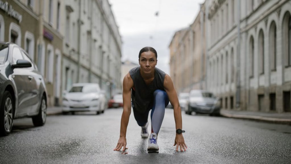 Woman in activewear poised for a run on a city street, symbolizing fitness and determination.