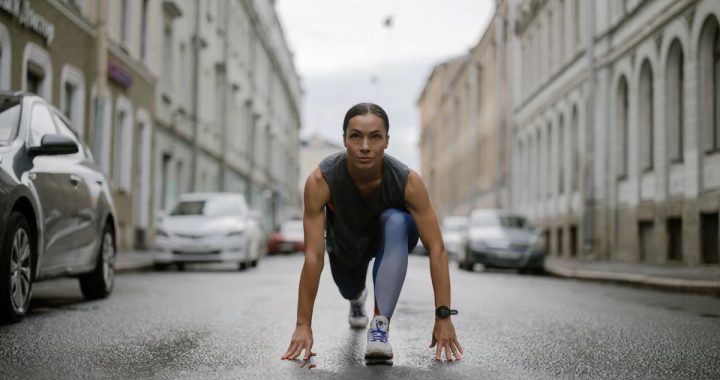 Woman in activewear poised for a run on a city street, symbolizing fitness and determination.